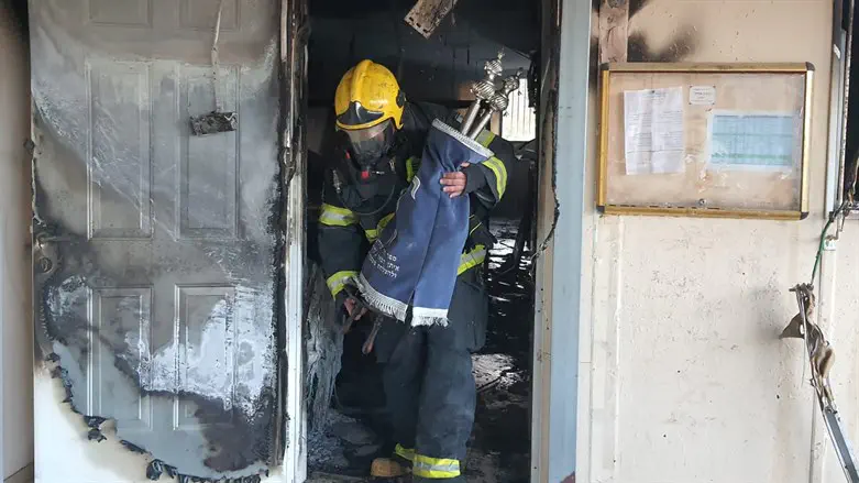 A firefighter takes one of the Torah scrolls out of the burning synagogue