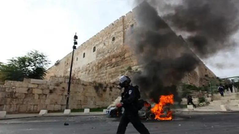 Policeman walks past car burnt by rioters, We
